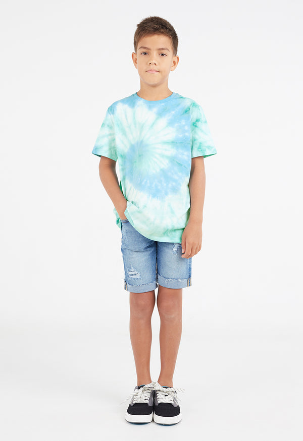 The young boy wears the Boys Aqua and Mint Spiral Tie-Dye T-Shirt by Gen Woo with denim shorts and sneakers