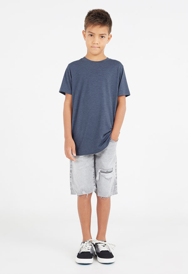 The young boy wears the Boys Classic Crew Neck Navy T-Shirt by Gen Woo with denim shorts and trainers