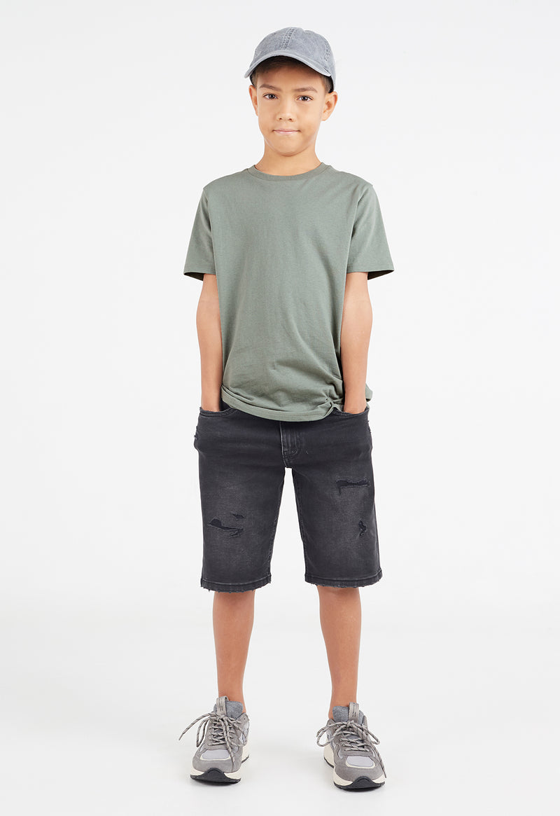The young boy wears the Boys Classic Crew Neck Sage Green T-Shirt by Gen Woo with shorts and trainers