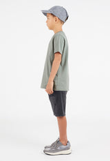 Side view as the young boy wears the Boys Classic Crew Neck Sage Green T-Shirt by Gen Woo with a baseball cap, shorts and trainers