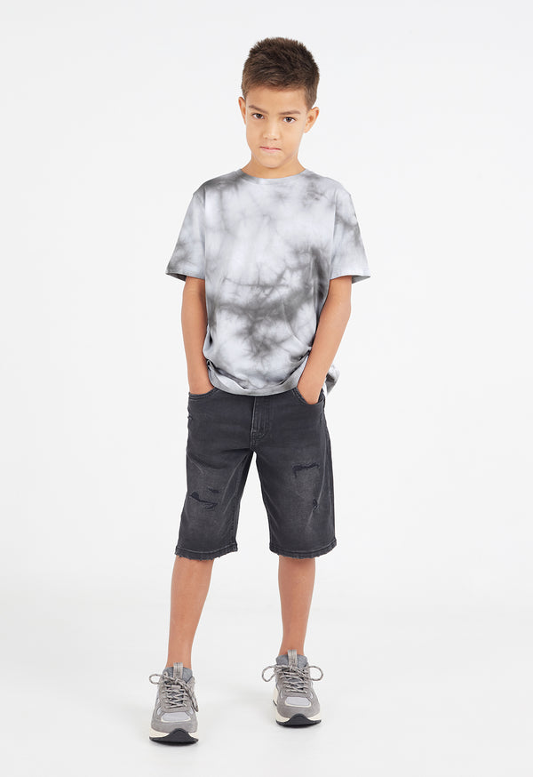 The young boy wears the Boys Grey Tie-Dye T-Shirt by Gen Woo with denim shorts and sneakers