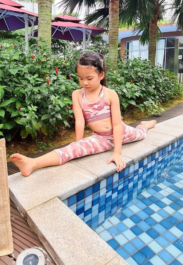 The young girl stretches poolside wearing the Pink Camo Girls Racer Crop Top by Gen Woo