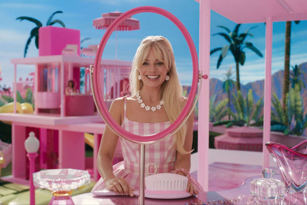 Margot Robbie in character as Barbie for the 2023 movie. She is pictured smiling, looking through a pink mirror. Image: Warner Bros.