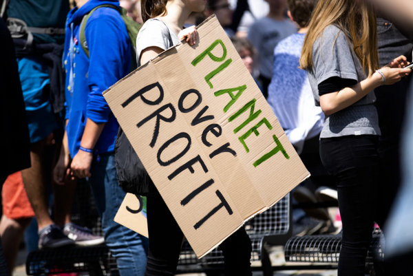 Greenwashing and climate campaigner holds up a cardboard sign reading ‘Planet over profit’.