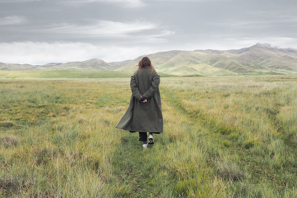 Back view of Amy Powney standing alone in an open field, silhouetted against a grey sky and rolling hills.