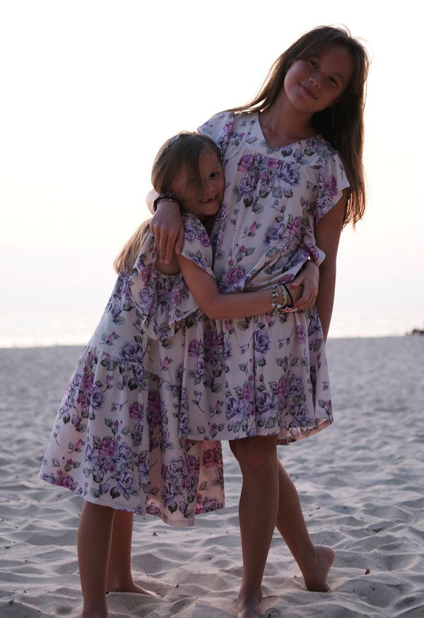 The two young girls wear the Pink and Purple Floral Bloom Tiered Girls Dress by Gen Woo