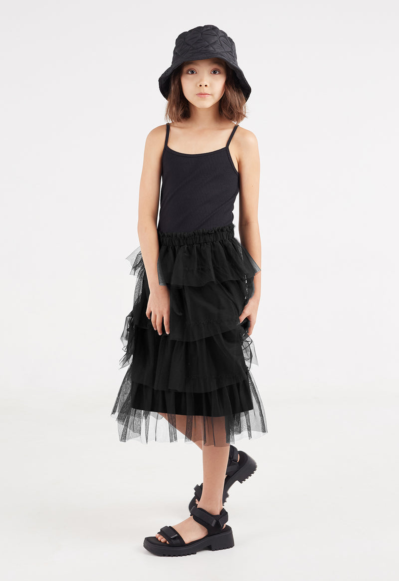The young girl wears the Black Tulle Girls Midi Skirt by Gen Woo with a cami top and chunky sandals