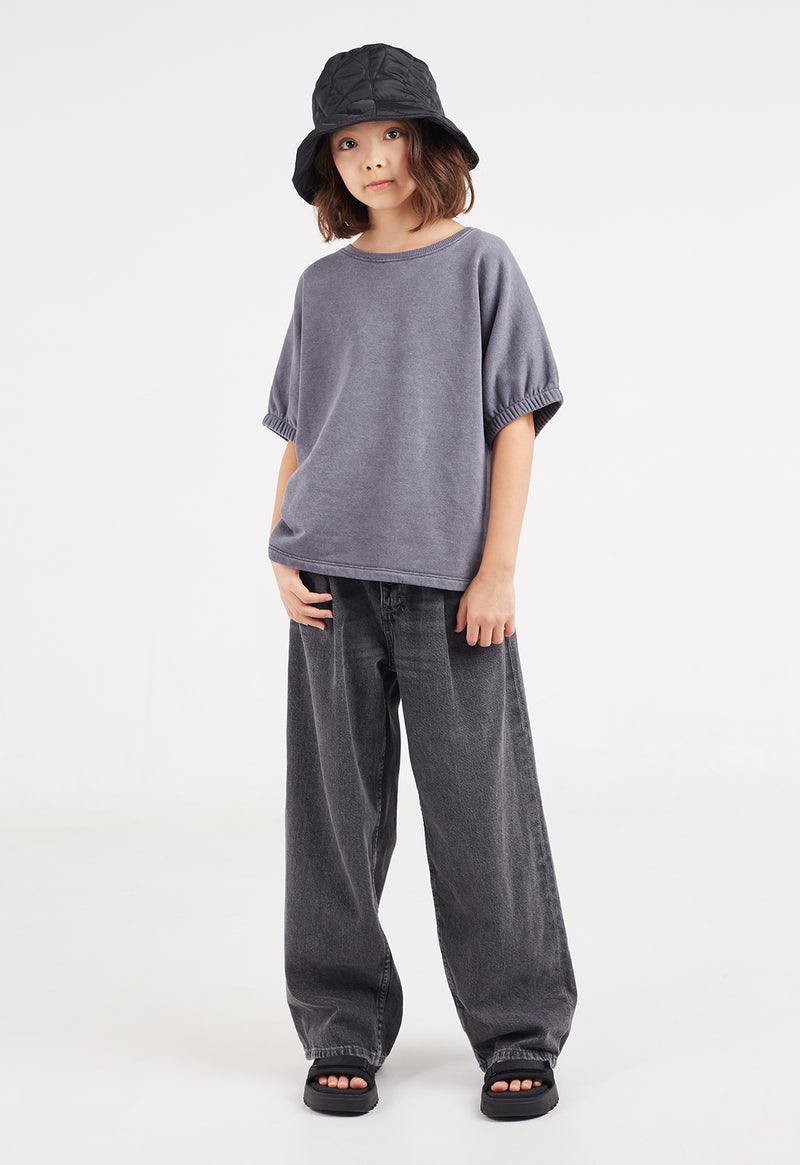 The young girl wears the Washed Grey Boxy Girls Sweater T-Shirt by Gen Woo with jeans and a bucket hat