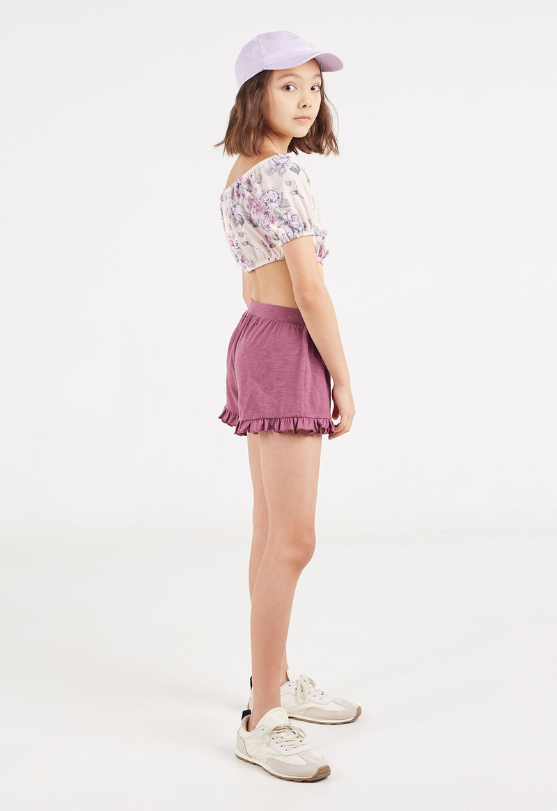 Side profile of the teen girl wearing the Damson Cotton Peplum Frill Girls Shorts by Gen Woo