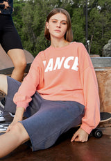 The model relaxes wearing the Salmon Cropped Slogan Sweater by Gen Woo