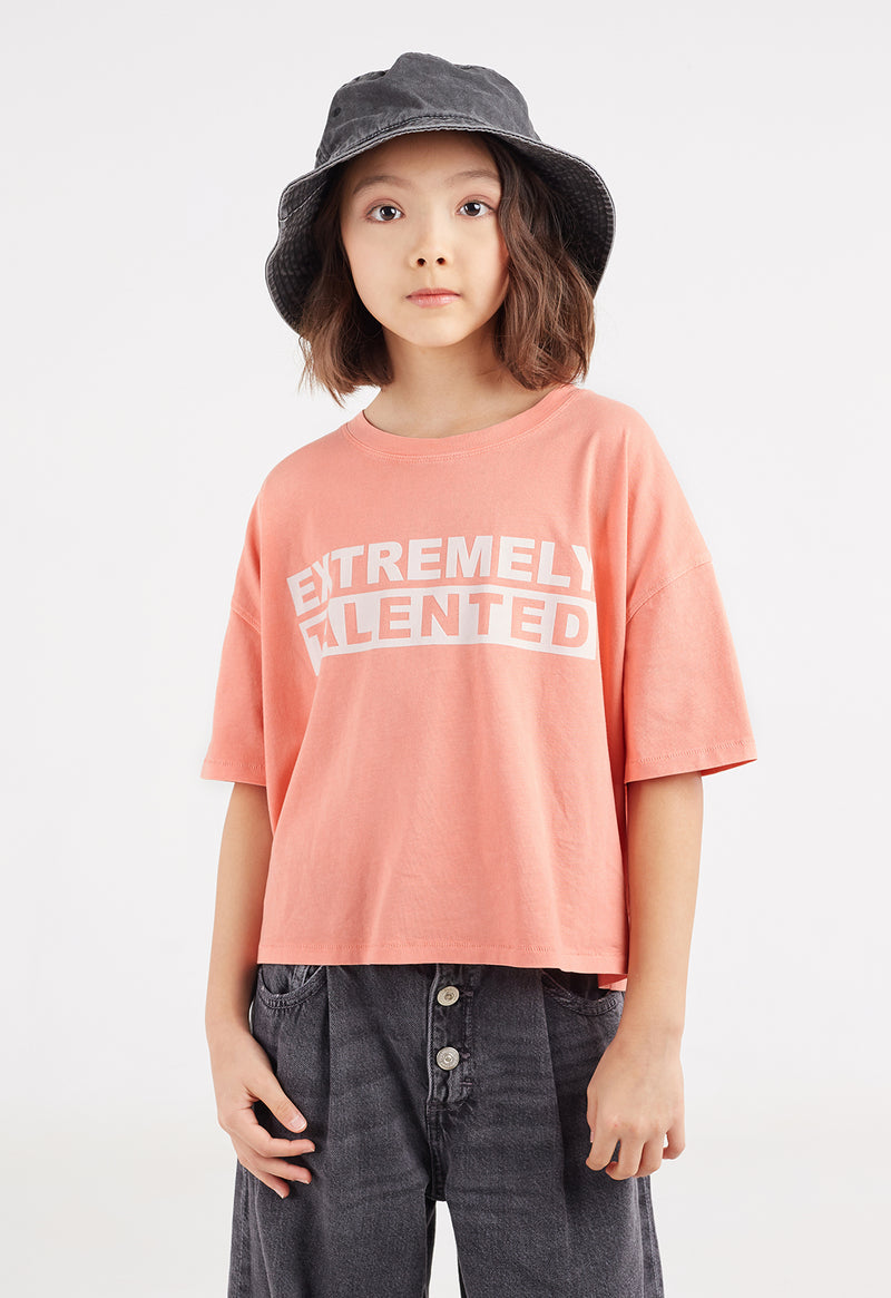 A close-up of teen girl wearing the Pink “Extremely Talented” Slogan Girls Boxy Cropped T-Shirt by Gen Woo