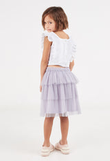 The young girl looks over her shoulder wearing the Purple Mesh Tiered Knee-Length Girls Skirt by Gen Woo