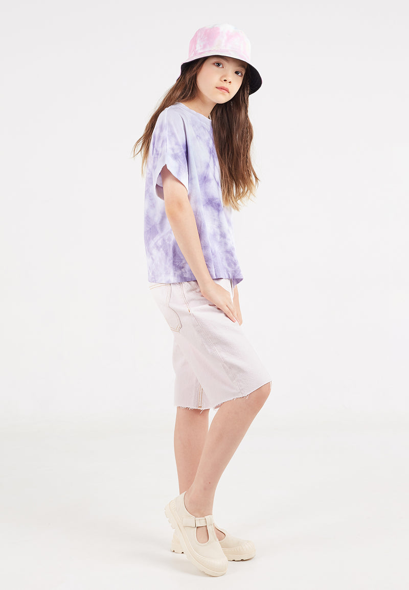 The teen girl wears the Purple and White Girls Tie-Dye T-Shirt by Gen Woo with denim shorts and a bucket hat