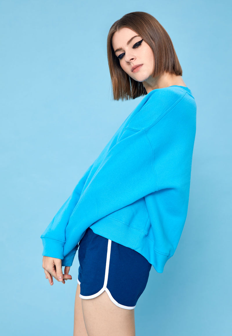 The model wears the Blue and White Retro Ladies Track Shorts by Gen Woo with a blue sweater