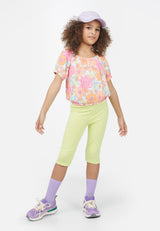The young girl wears the Neon Lime Cropped Girls Leggings by Gen Woo with a floral top and pastel accessories 