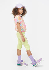 The young girl wears the Neon Lime Cropped Girls Leggings by Gen Woo with trainers and a baseball hat 