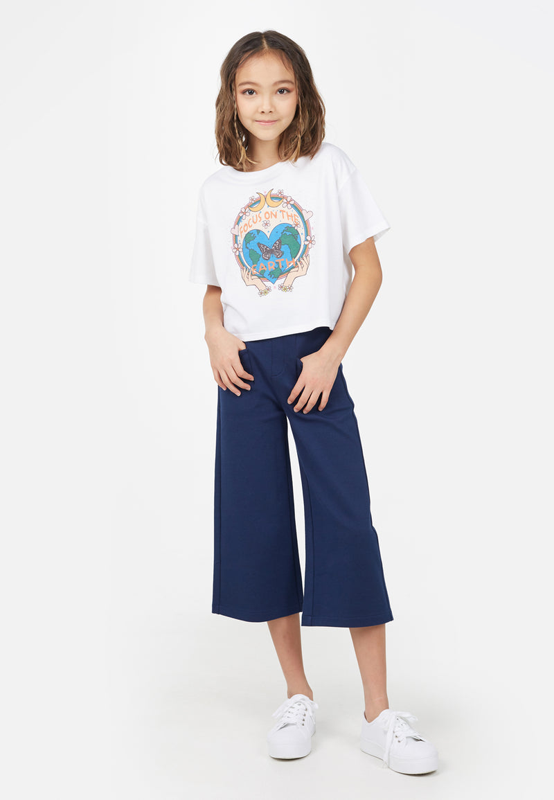 The young girl wears the “Focus on the Earth” Cropped Graphic Tee by Gen Woo with cropped flared trousers 