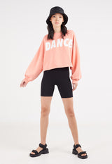  The model wears the Salmon Cropped Slogan Sweater by Gen Woo with a bucket hat, cycling shorts and sandals