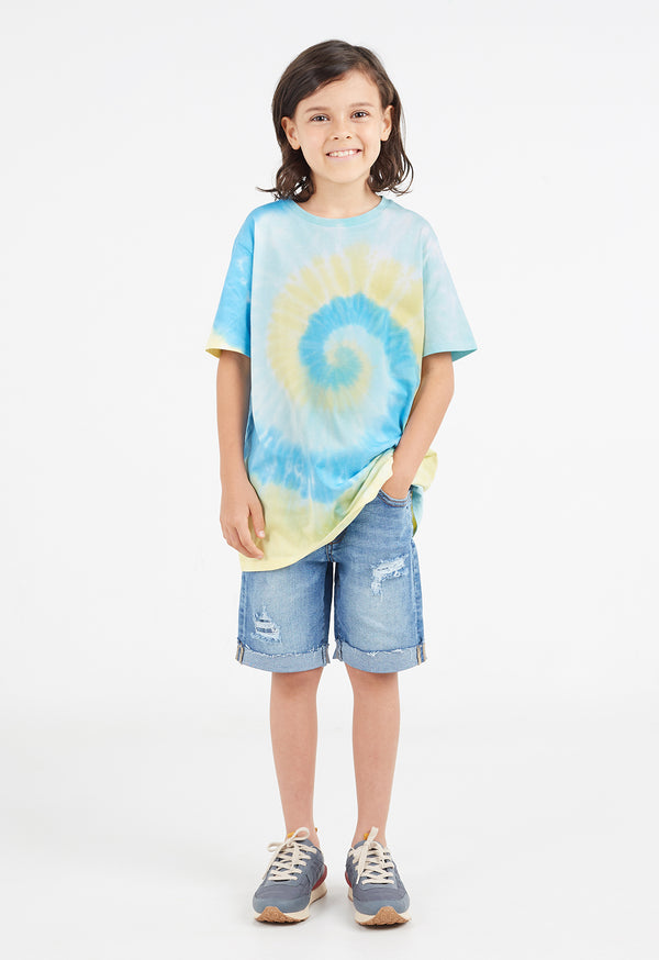 The young boy wears the Boys Blue and Yellow Spiral Tie-Dye T-Shirt by Gen Woo with denim shorts and sneakers