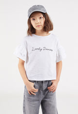 The young girl wears the “Lovely Princess” Broderie Trim Girls Crop Top by Gen Woo with a baseball cap and jeans