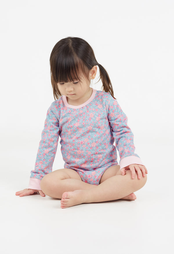 The young girl sits on the floor wearing the Ditsy Floral Print Long Sleeve Babygrow by Gen Woo