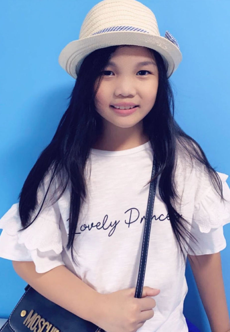 The young girl wears the “Lovely Princess” Broderie Trim Girls Crop Top by Gen Woo with a sunhat
