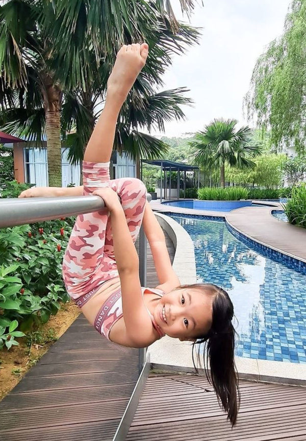 The young girl hangs upside down poolside wearing the Pink Camo Print Girls Leggings by Gen Woo