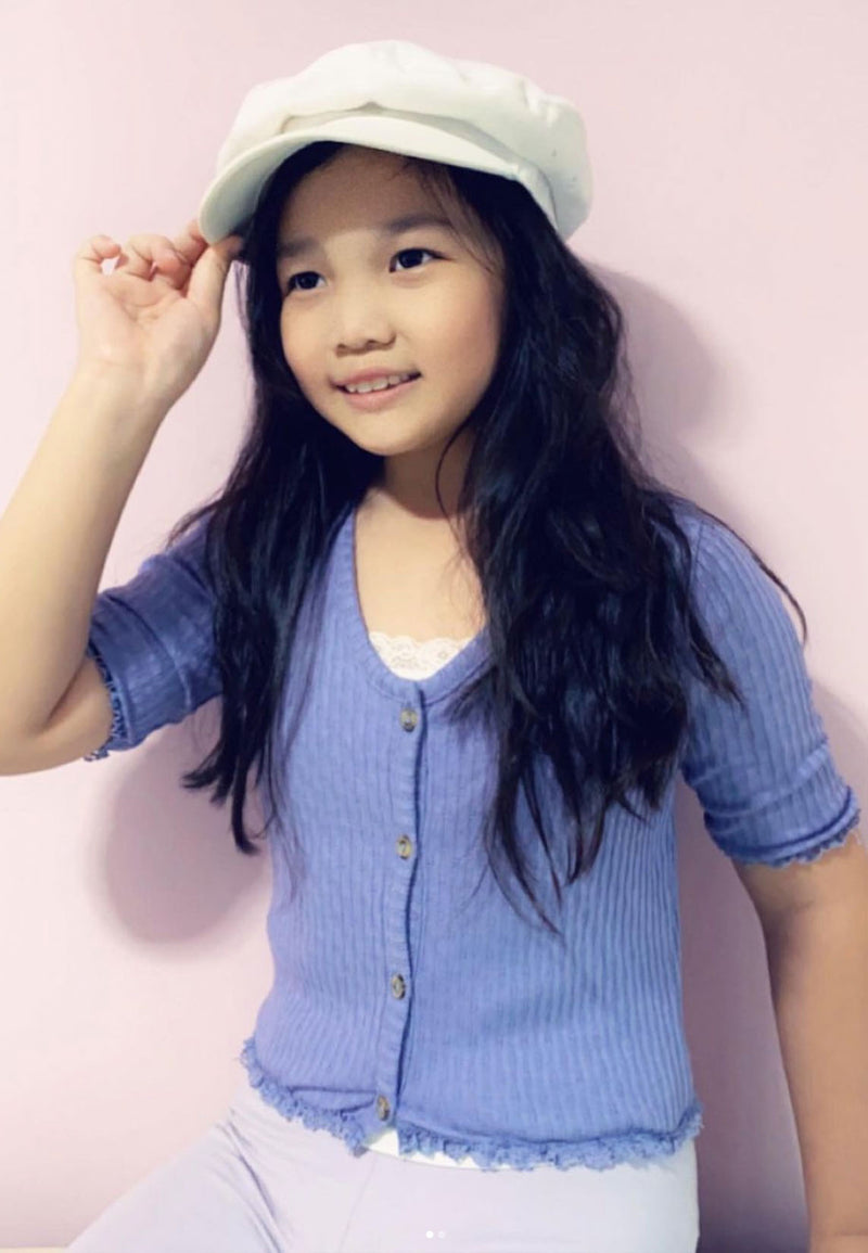 The young girl wears the Purple Pointelle Henley Girls Cropped Top by Gen Woo