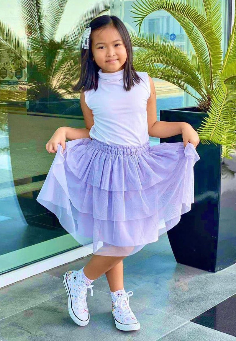 The young girl curtseys wearing the Purple Mesh Tiered Knee-Length Girls Skirt by Gen Woo