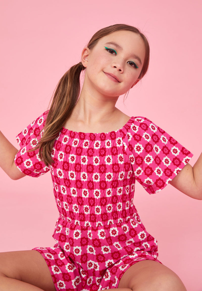 Teenage girl sits wearing the Retro Floral Print Pink Checkerboard Girls Playsuit by Gen Woo