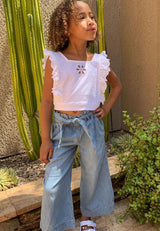 The young girl wearing the Broderie Trim Girls Flutter Crop Top by Gen Woo with denim trousers